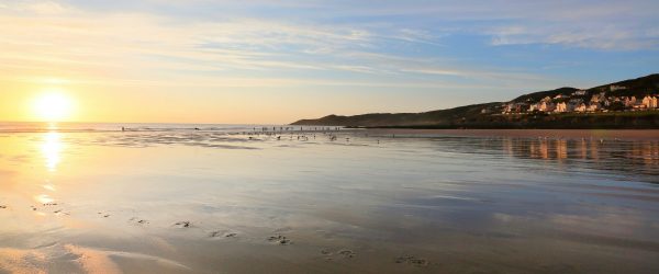 empty beach with a few surfers and dog walkers in the evening, uk